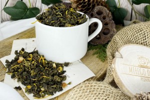 Ciemnozielone zwinięte liście herbaty oolong wymieszane z pomarańczową skórką żółtymi płatkami nagietka i kawałkami cynamonu