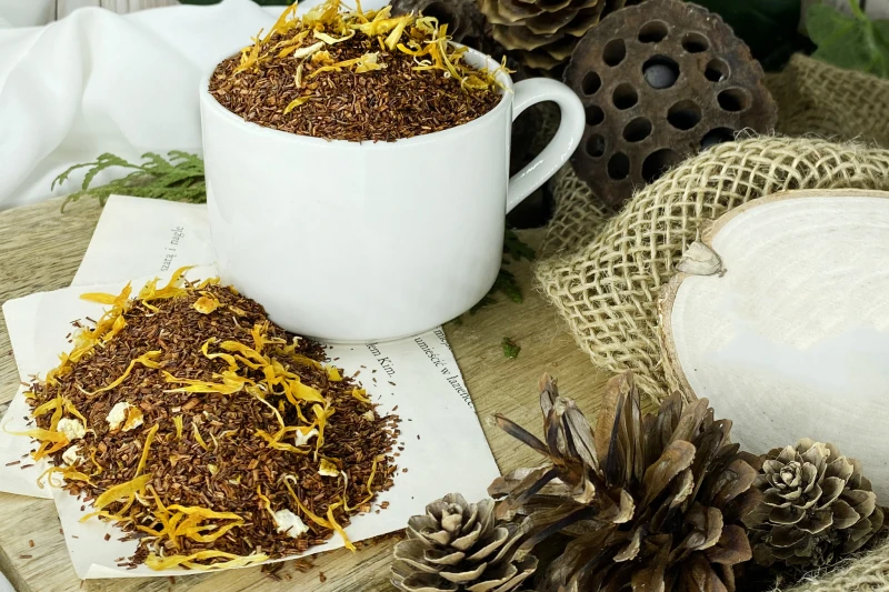 Słoneczne płatki nagietka oraz kawałki skórki pomarańczy w drobnych igiełkach herbaty rooibos